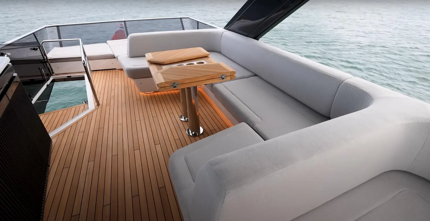 Luxury yacht deck featuring a plush grey sofa, timber table, and polished detailing against a serene water backdrop.